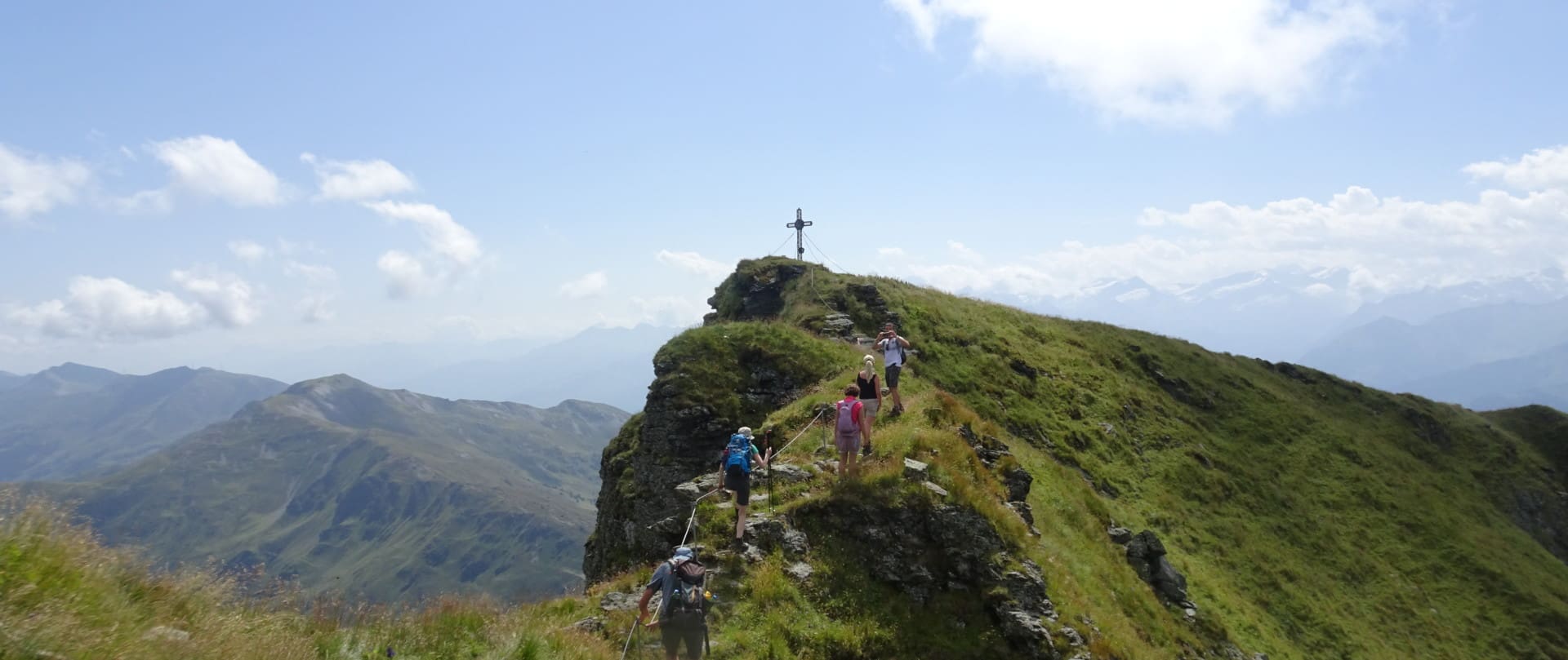 Wanderer auf dem Gipfel des Gaisstein genießen die Aussicht neben einem Kreuz, das hoch über dem Tal steht, mit einer grünen Bergkette im Hintergrund