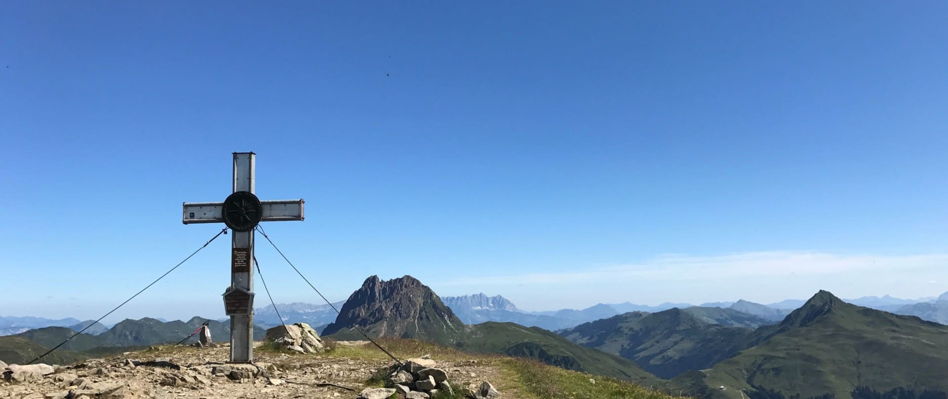 Ein robustes Gipfelkreuz auf dem Wildkogel-Panoramaweg ragt in den strahlend blauen Himmel